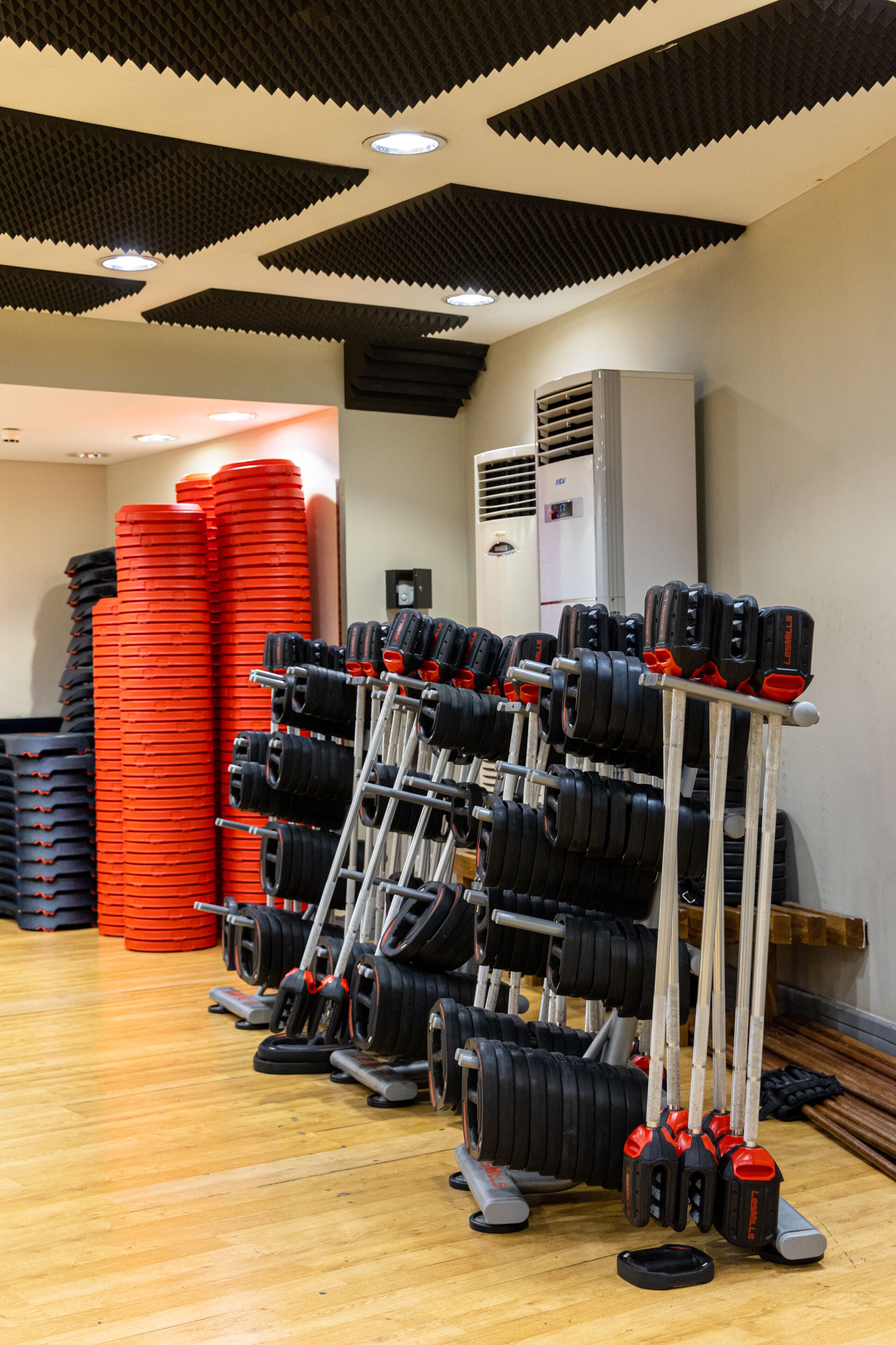 A gym with weightlifting equipment, including dumbbells and weight plates, and an air conditioning unit on the wall.