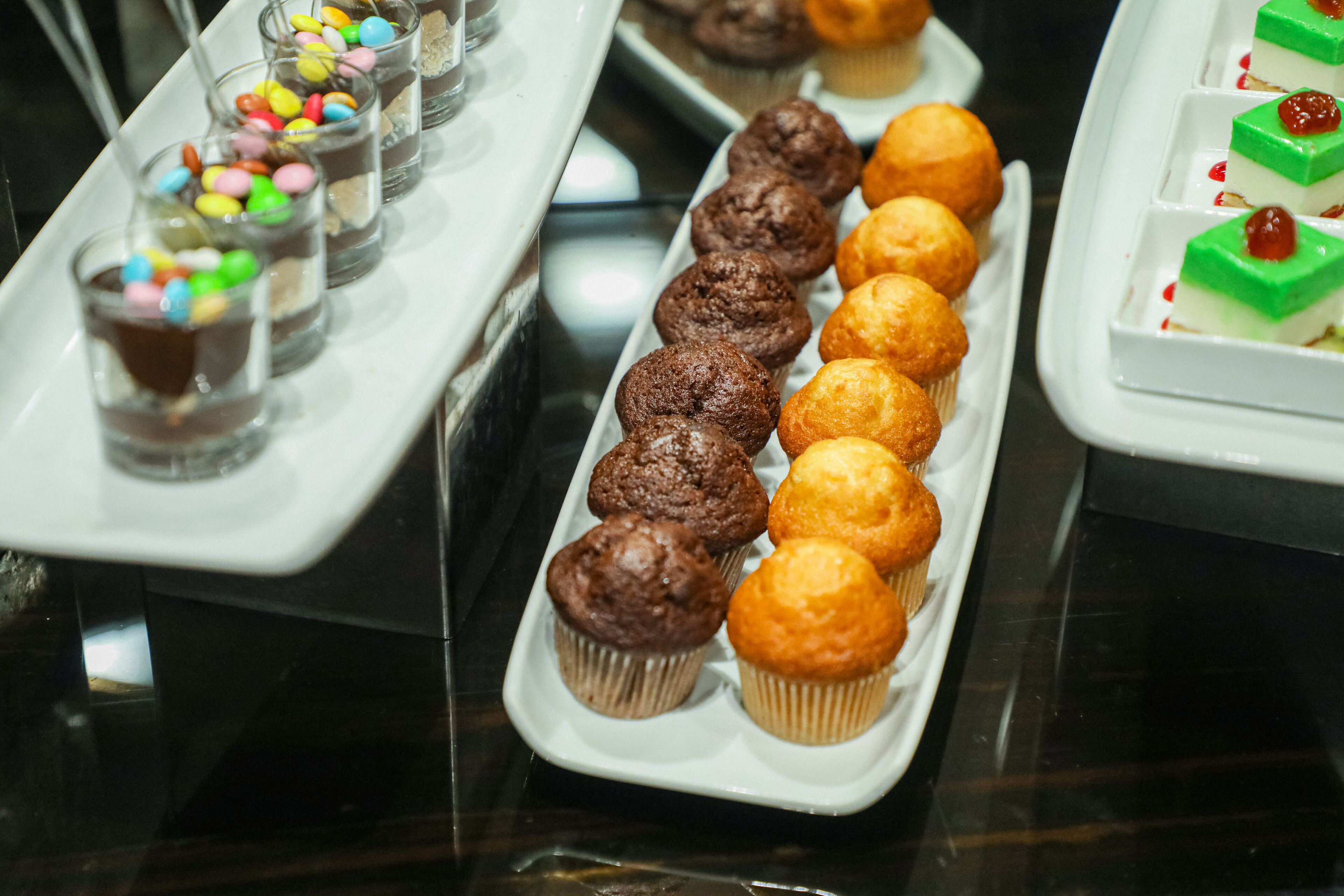 Verschiedene Desserts auf Tabletts, darunter Cupcakes und kleine Gläser mit Süßigkeiten.