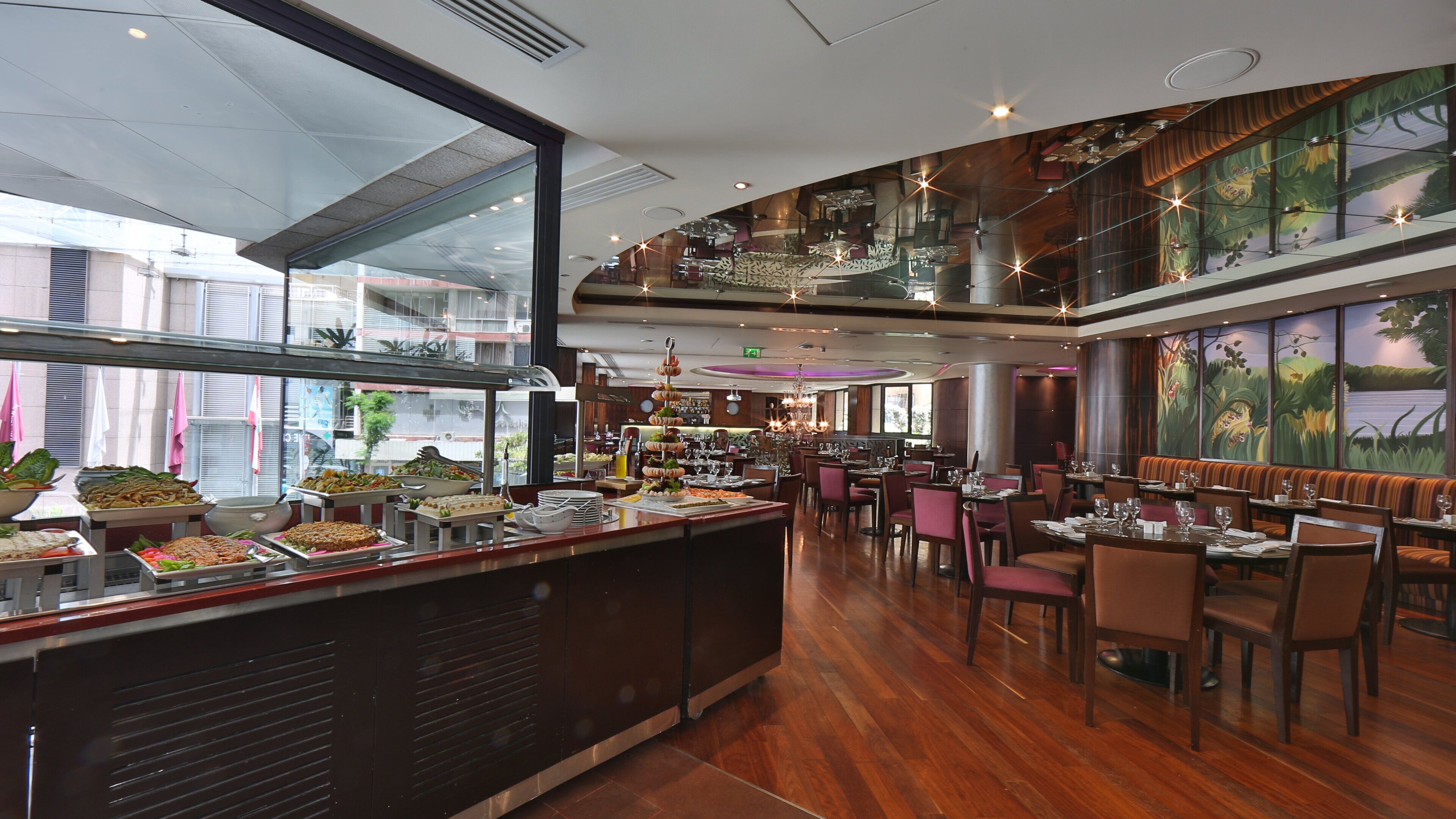 A spacious restaurant with a buffet area, high ceilings, and a view of the city through large windows.