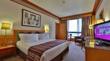 A hotel room with a bed, a desk with a computer, a TV, and a window with curtains.
