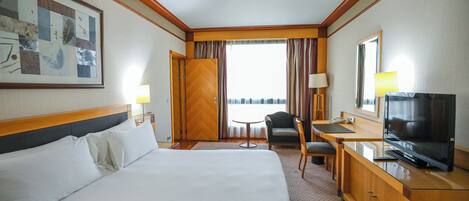 A hotel room with a large bed, a desk with a television, a chair, and a window with curtains.