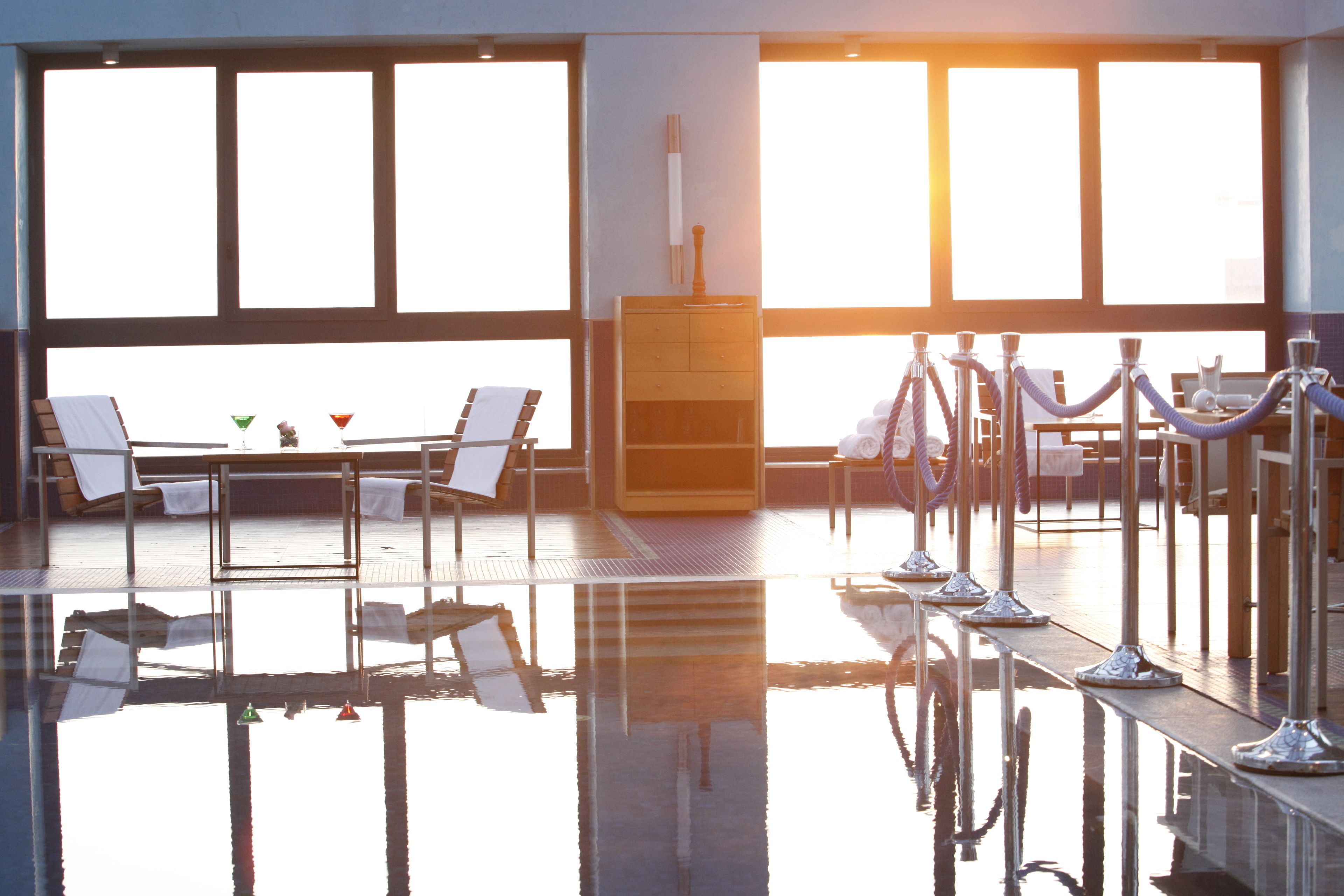 Una habitación soleada con piscina, sillas de descanso y un mueble de madera.