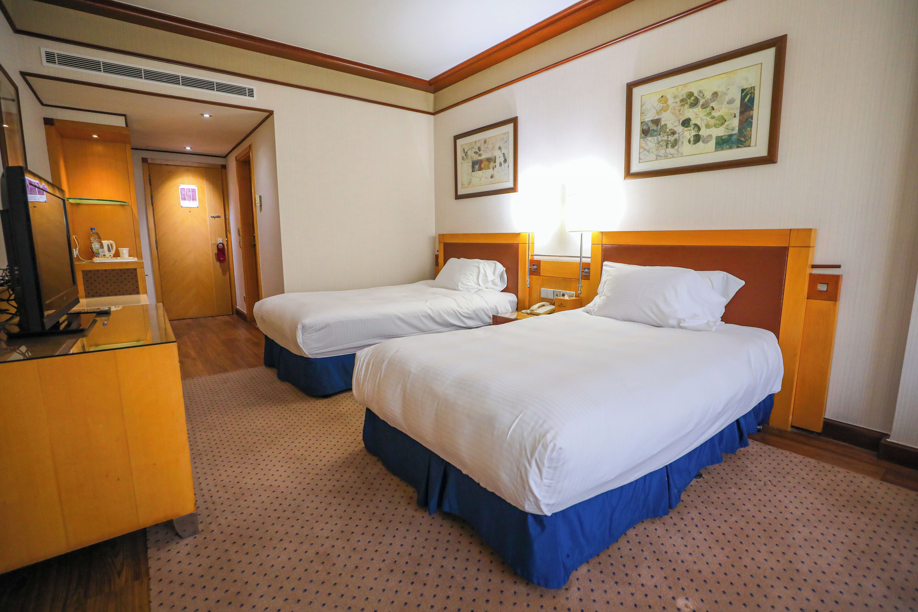 A hotel room with two beds, a desk, and a mirror. There is a door leading to another room.