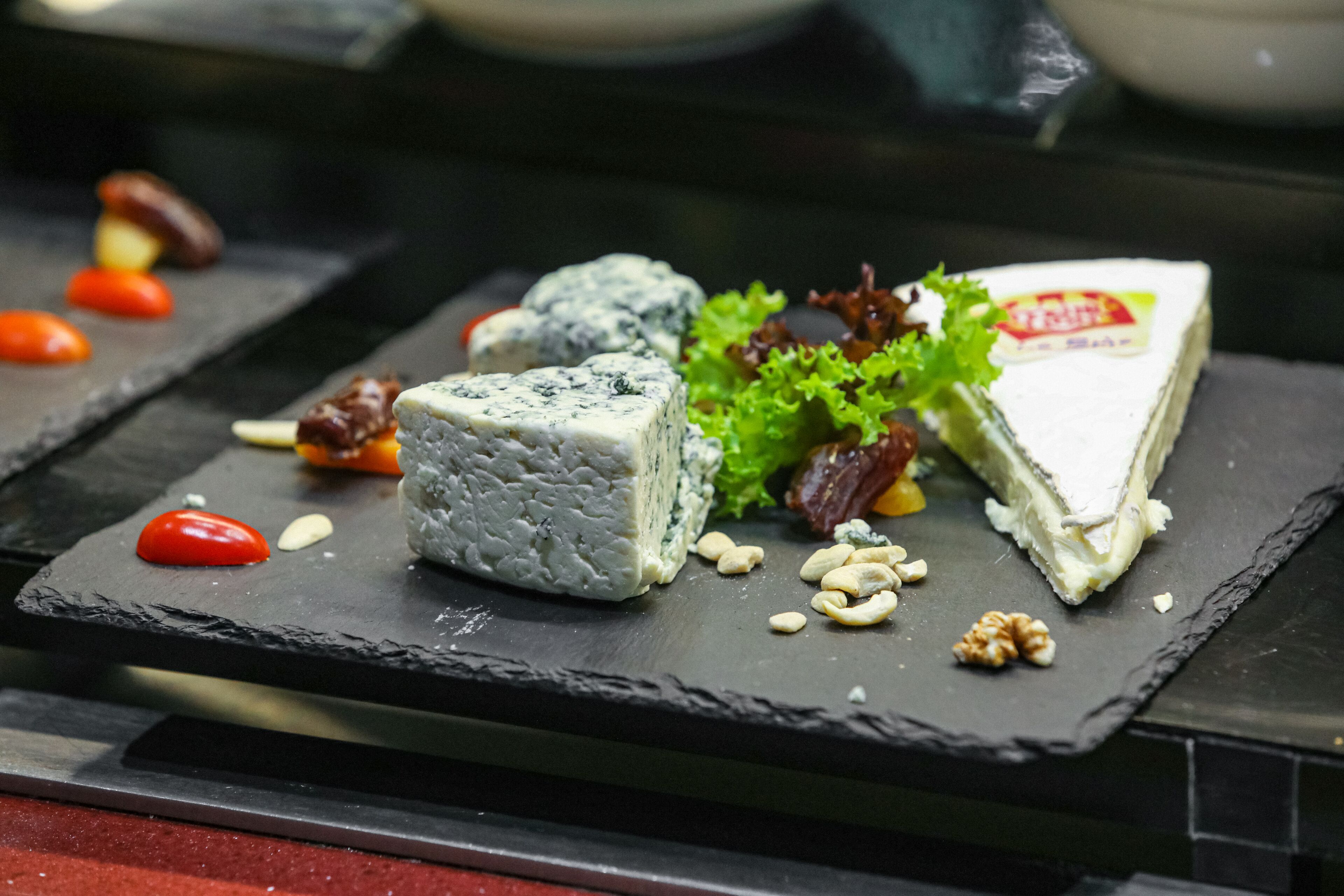 A slate serving board with a variety of cheeses, nuts, and vegetables.