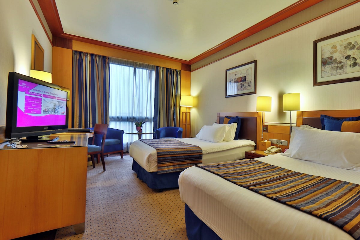 A hotel room with two beds, a desk with a television, and a chair.