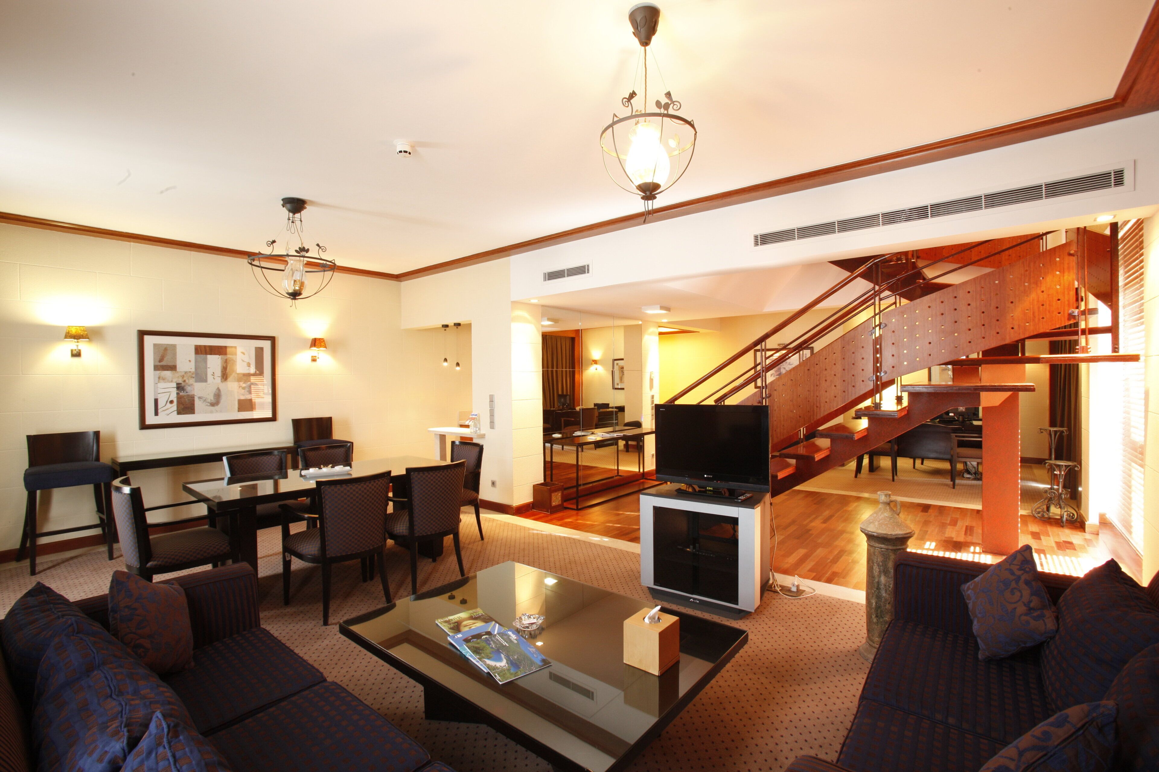 A spacious living area with a dining table, comfortable seating, a flat-screen TV, and a staircase leading to an upper level.