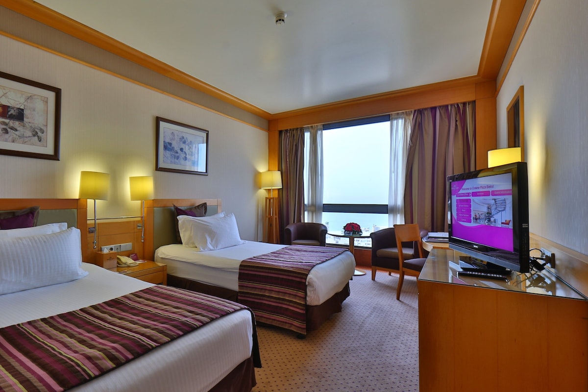 A hotel room with two beds, a desk with a computer, and a view of the city.