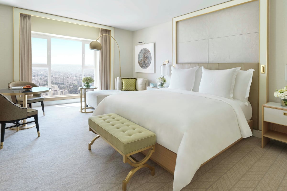 A hotel room with a large bed, a desk with a chair, a view of the city, and a window with curtains.