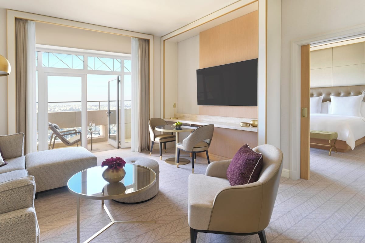 A modern hotel room with a balcony, a dining area, a bed, and a TV.