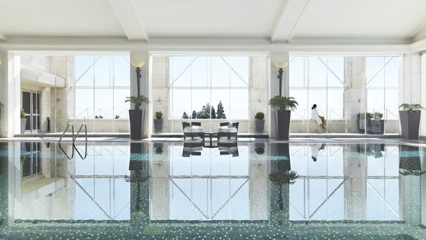 A spacious indoor swimming pool with clear glass walls, large windows, and potted plants.