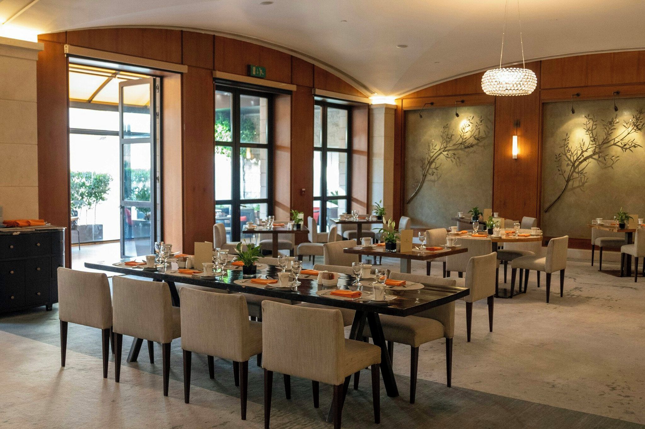 A spacious dining area with multiple tables and chairs, large windows, and a decorative wall.