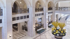 A multi-level hotel lobby with marble floors, a grand piano, seating areas, and a staircase.