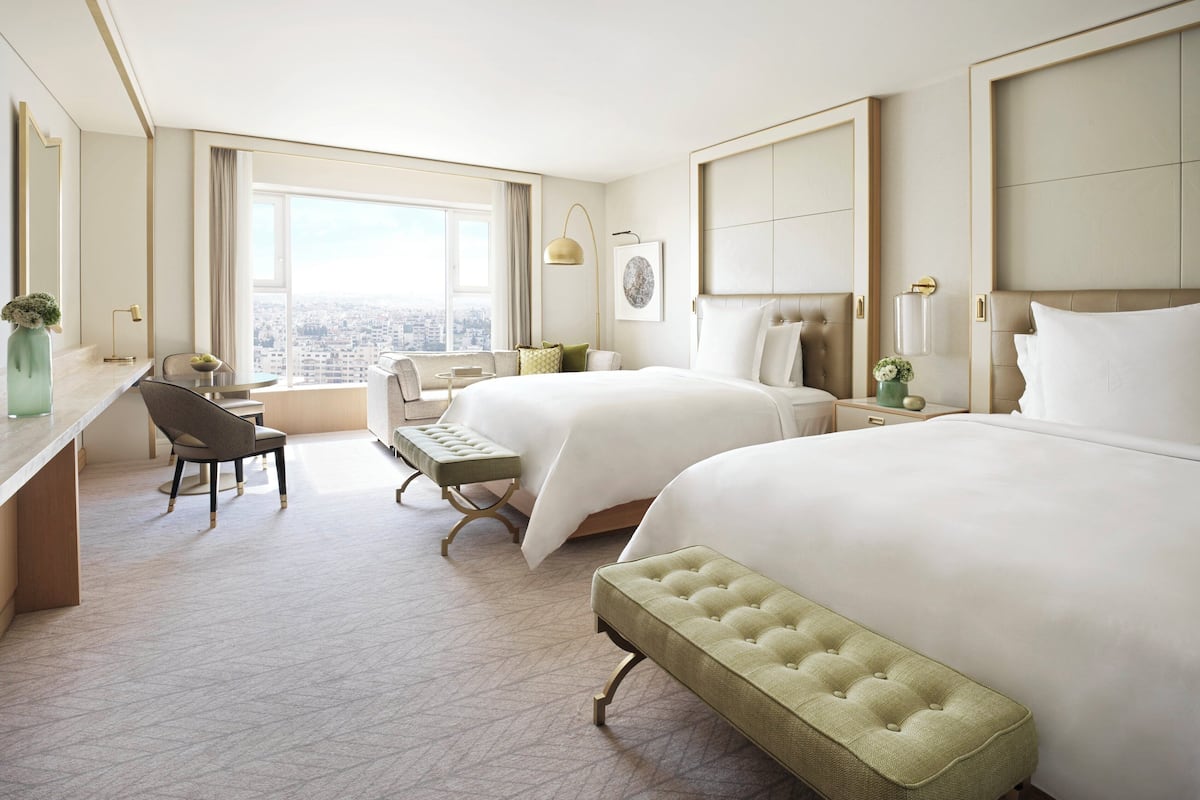 A hotel room with two beds, a desk, a chair, and a view of the city.
