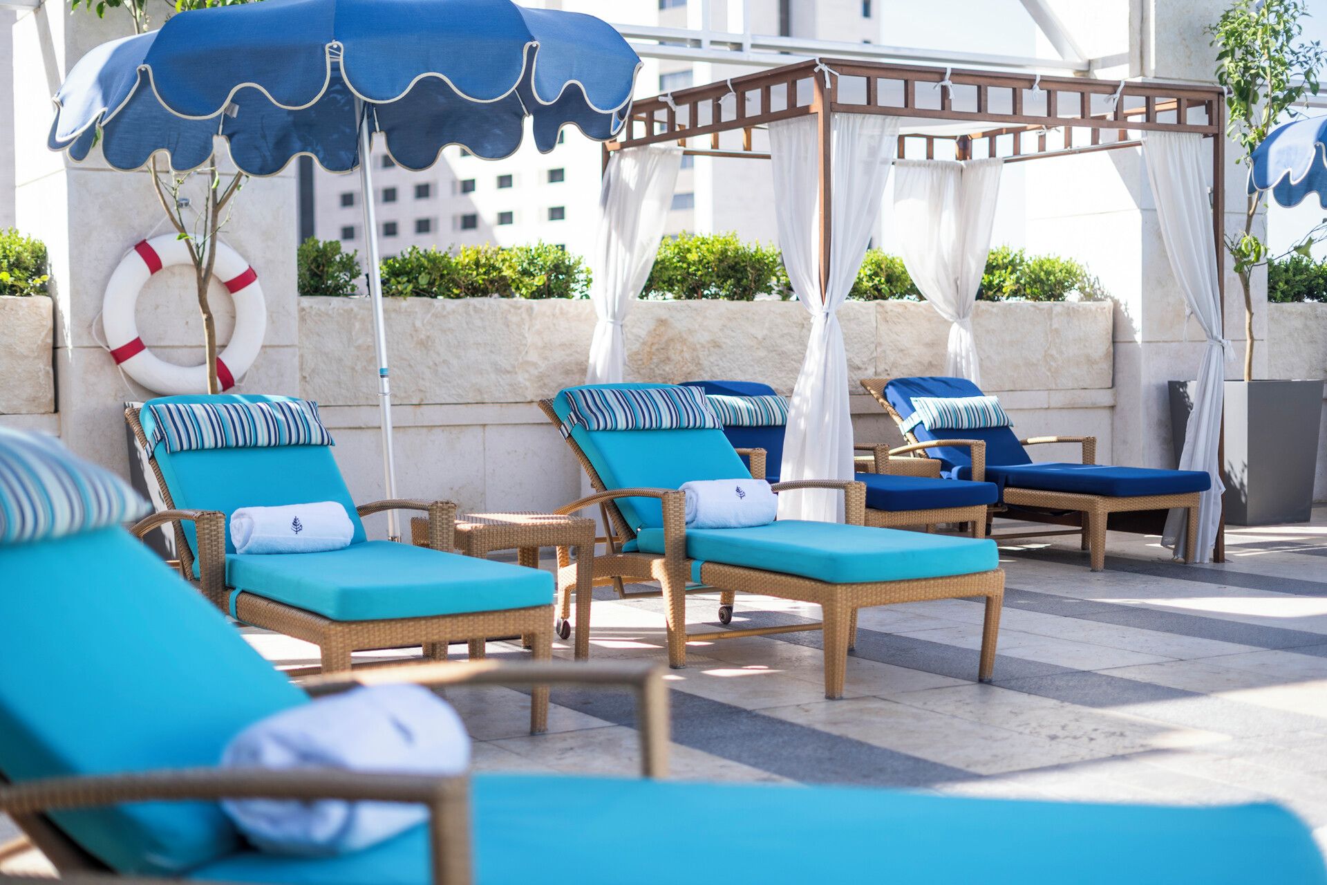 A rooftop lounge area with wicker lounge chairs, blue cushions, and a pergola with white curtains.