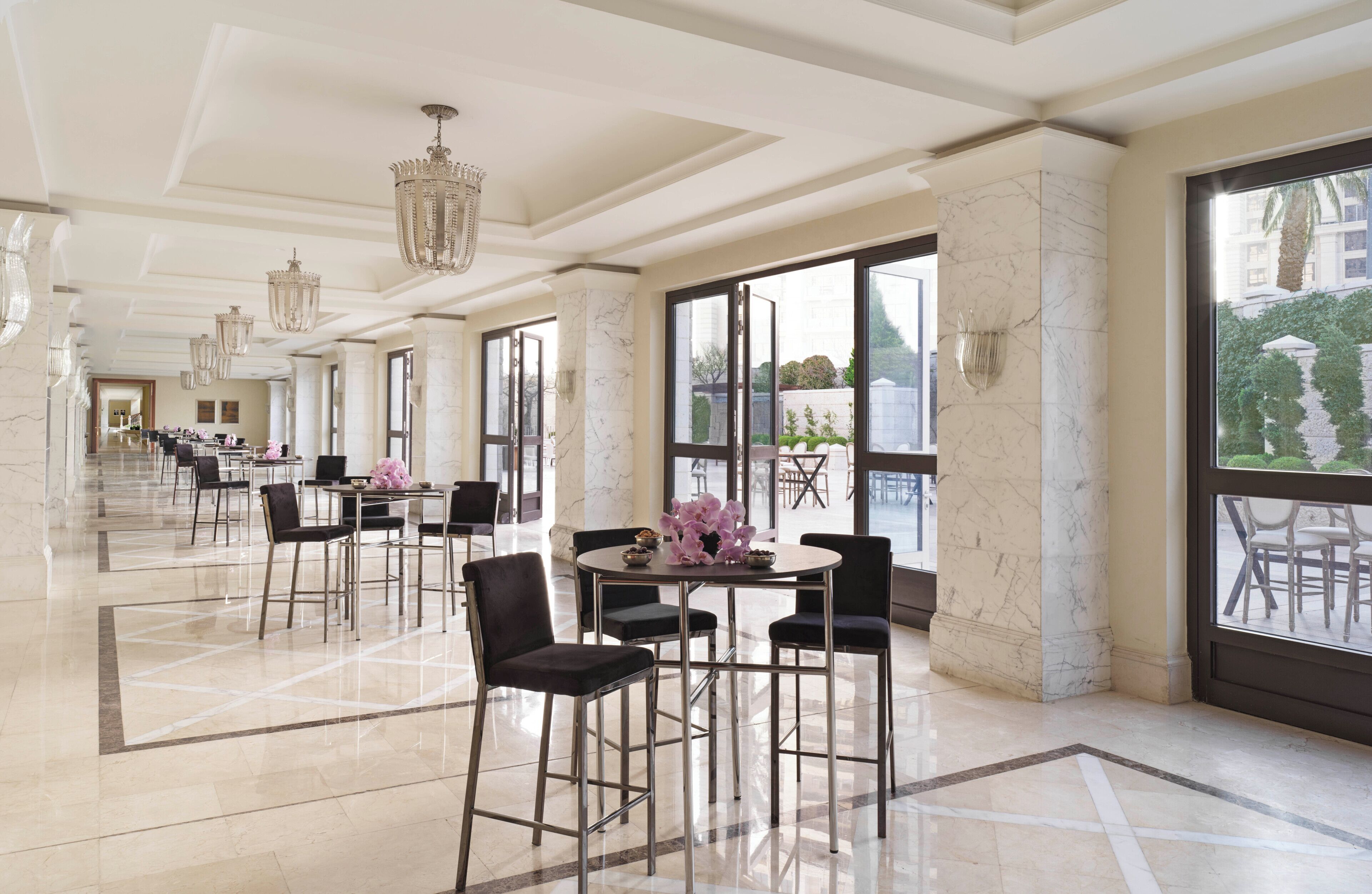 A spacious hotel lobby with marble flooring, modern furniture, and large windows offering views of the outdoors.