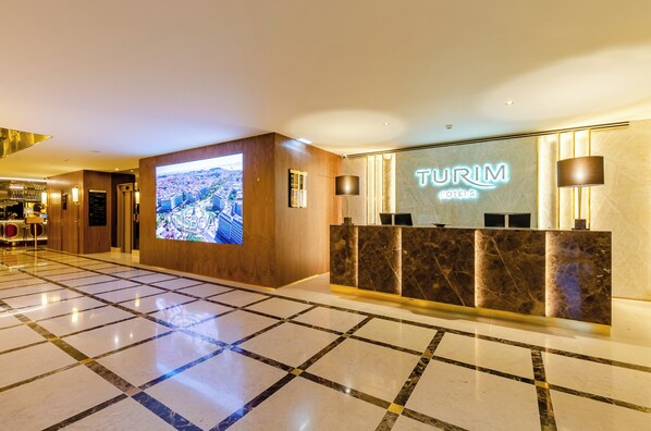 A hotel reception area with a large digital screen displaying a cityscape, a reception desk, and a polished marble floor. - TURIM Lisboa Hotel (Lisbon)