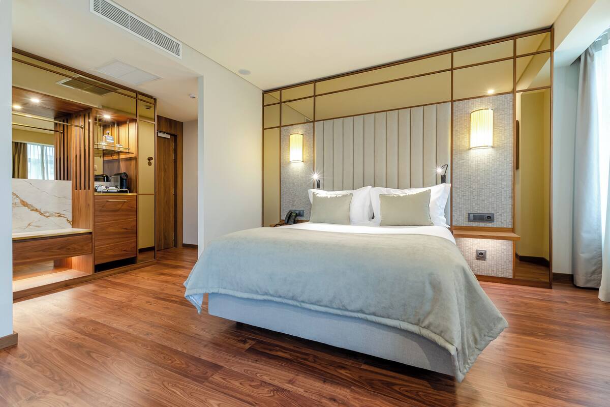 A hotel room with a large bed, wooden wardrobe, bedside lamps, and a marble-topped nightstand.