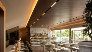 Un restaurante moderno con suelo de madera, mesas redondas y sillas tapizadas en verde.