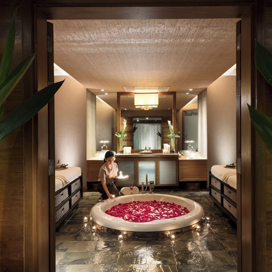 A bathroom with a large bathtub filled with rose petals, a sink, and a mirror.
