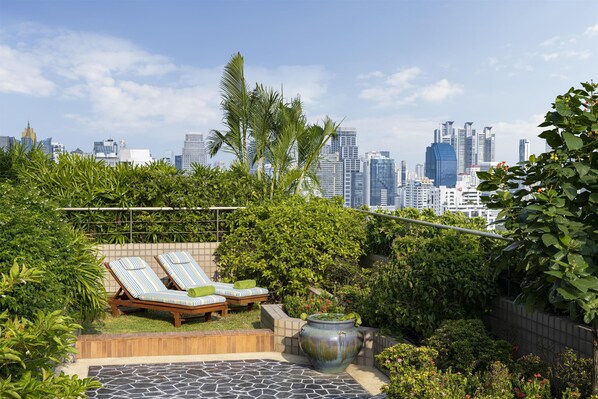 Un jardín en la azotea con sillones de descanso, una maceta decorativa grande y un horizonte urbano de fondo.