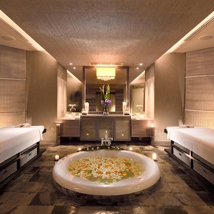 A spa room with two beds, a large bathtub filled with water and flowers, and a central sink area.