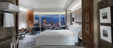 Een hotelkamer met een groot bed, een bureau, een stoel, een bureaulamp, uitzicht op de stad en een bad.