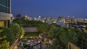 A rooftop patio with a dining table, chairs, and a view of a city skyline at dusk. - Conrad Bangkok (Bangkok)