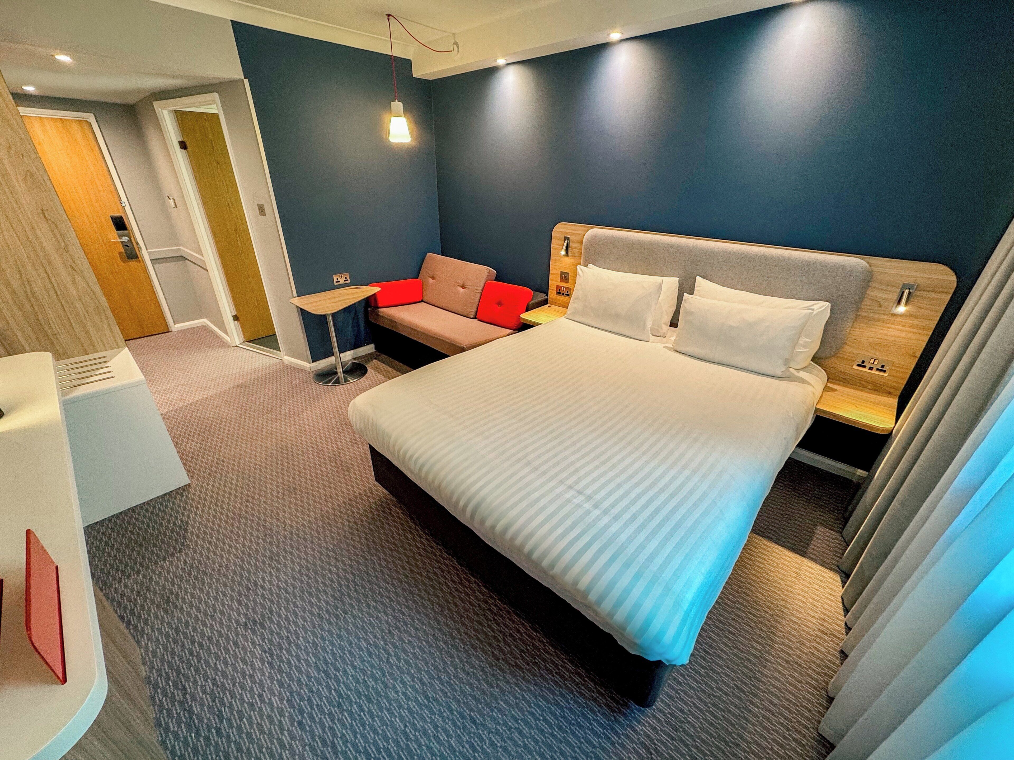 A modern hotel room with a large bed, a small table, a sofa, and a bathroom area.