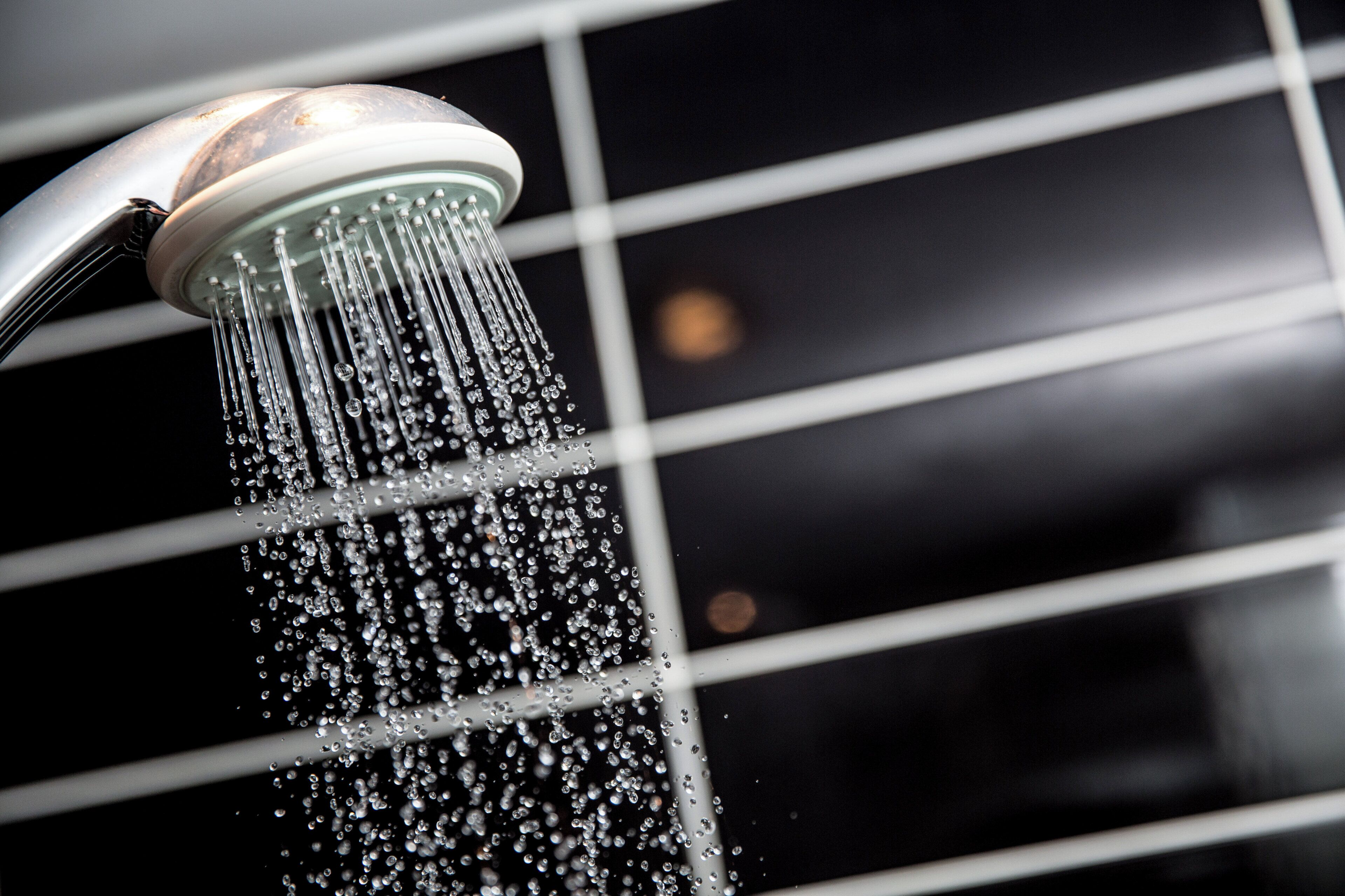 A showerhead with water flowing down a tiled wall.