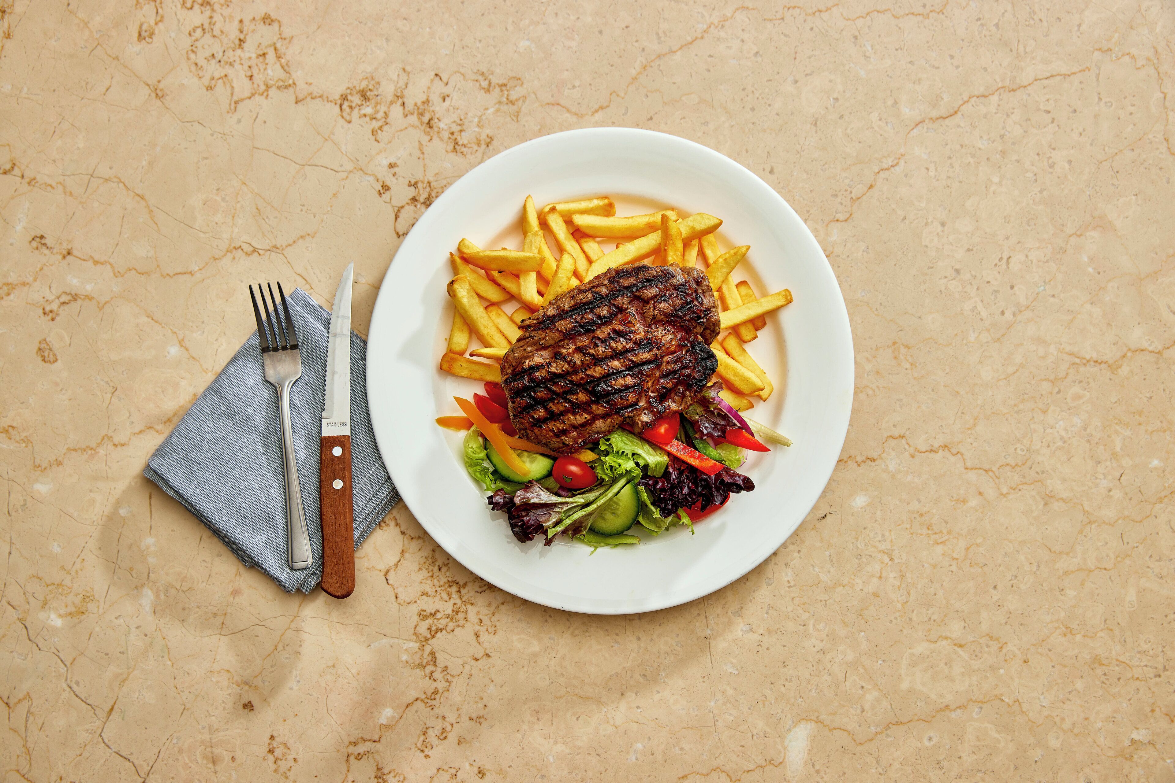 A plate with grilled meat, fries, and a salad on a marble surface.