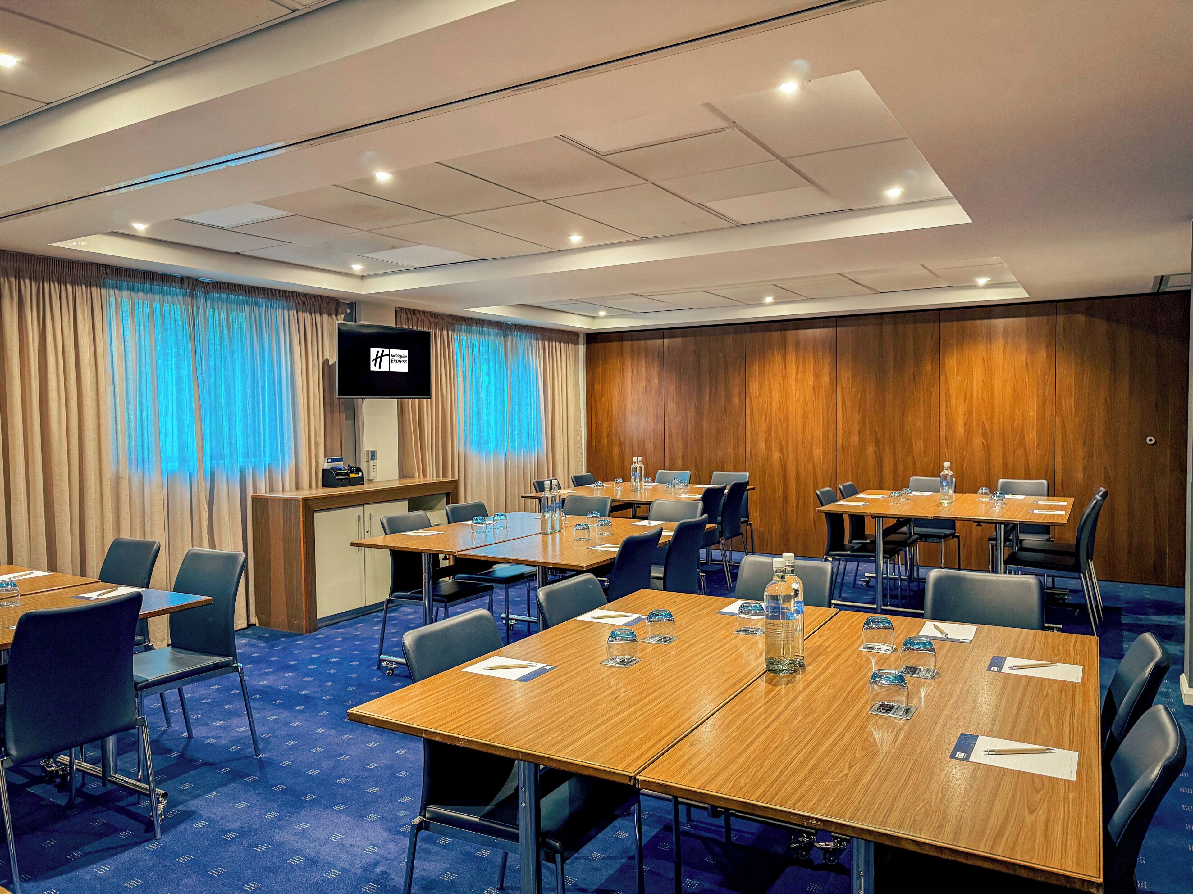 A conference room with multiple tables, chairs, a television screen, and a wooden panel wall.