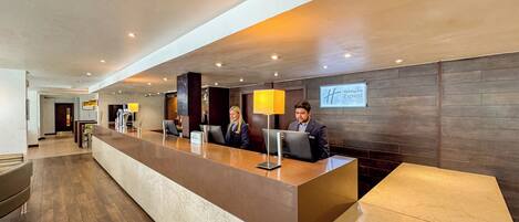 A hotel reception desk with a modern design, a reception area, and a sign indicating it's a Holiday Inn Express.