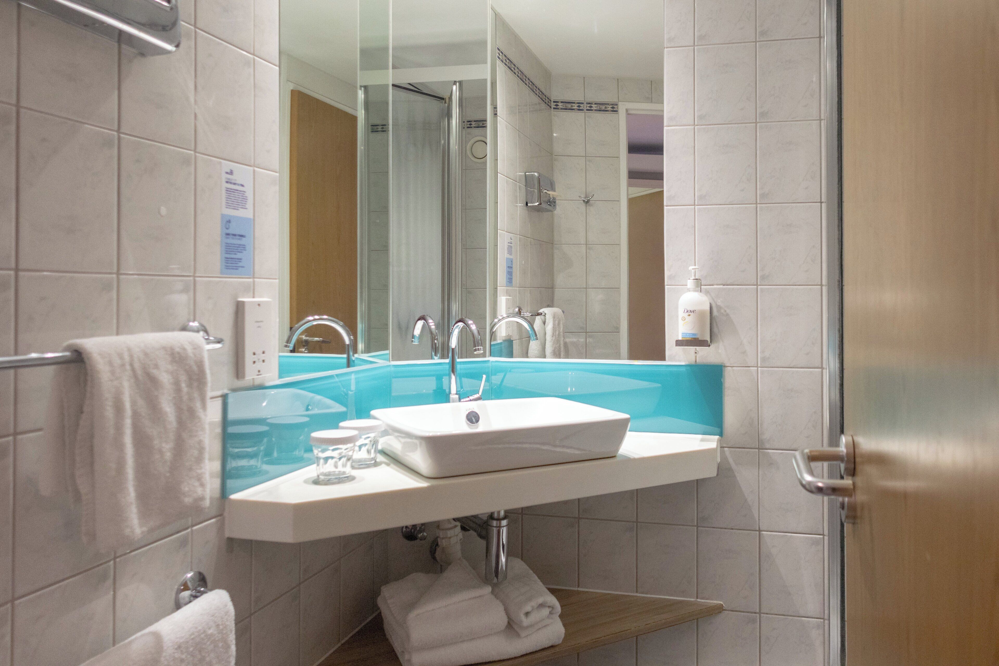 A bathroom with a glass-enclosed shower, a white sink, and a wooden shelf.