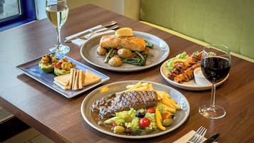 A dining table with three plates of food, two glasses of wine, and cutlery.