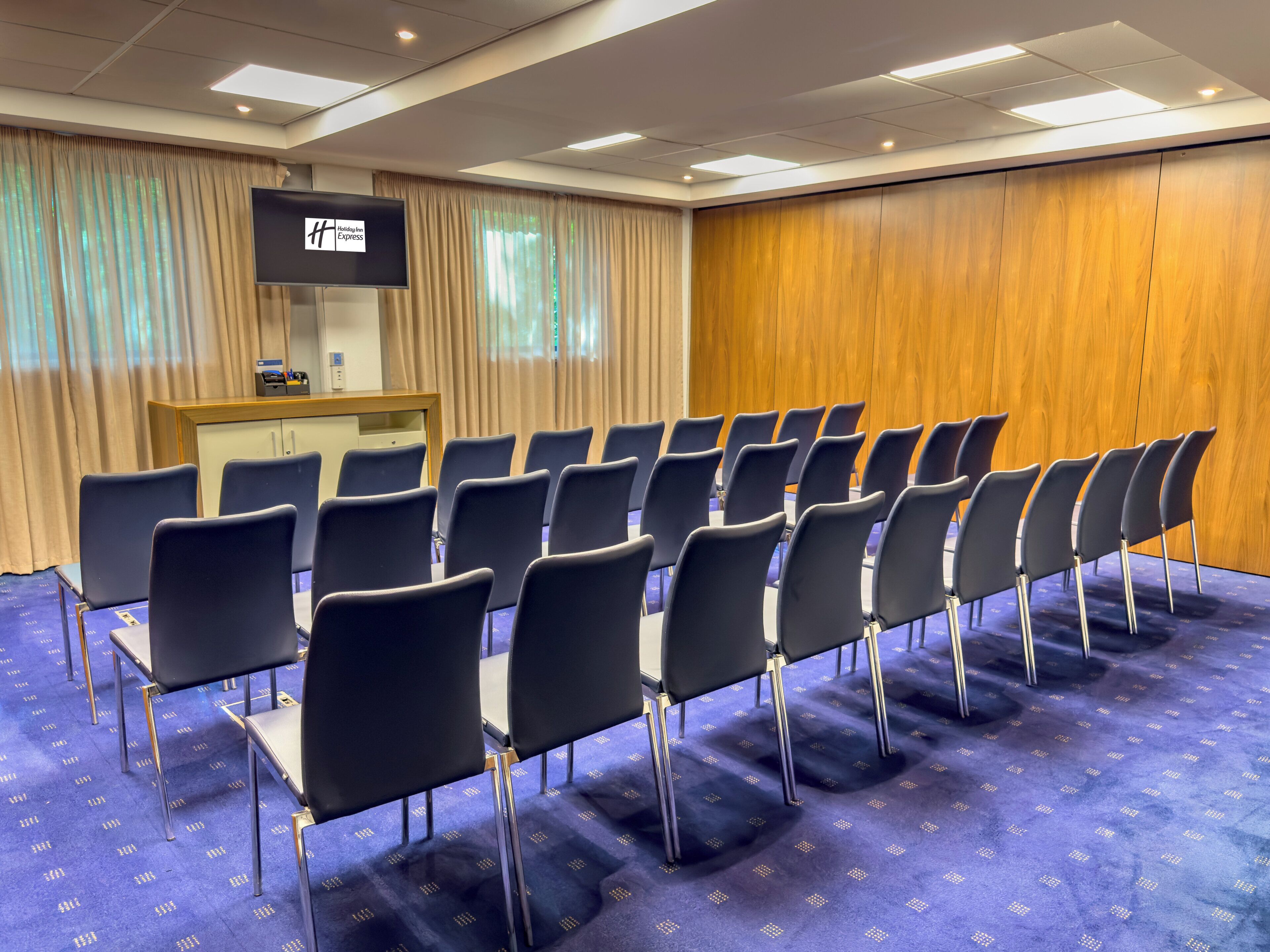 Uma sala de conferências com fileiras de cadeiras, um pódio e uma tela de televisão.