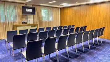 Uma sala de conferências com fileiras de cadeiras, um pódio e uma tela de televisão.