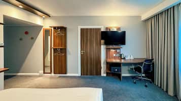 A hotel room with a bed, a desk with a chair, a TV, and a wardrobe with hangers.