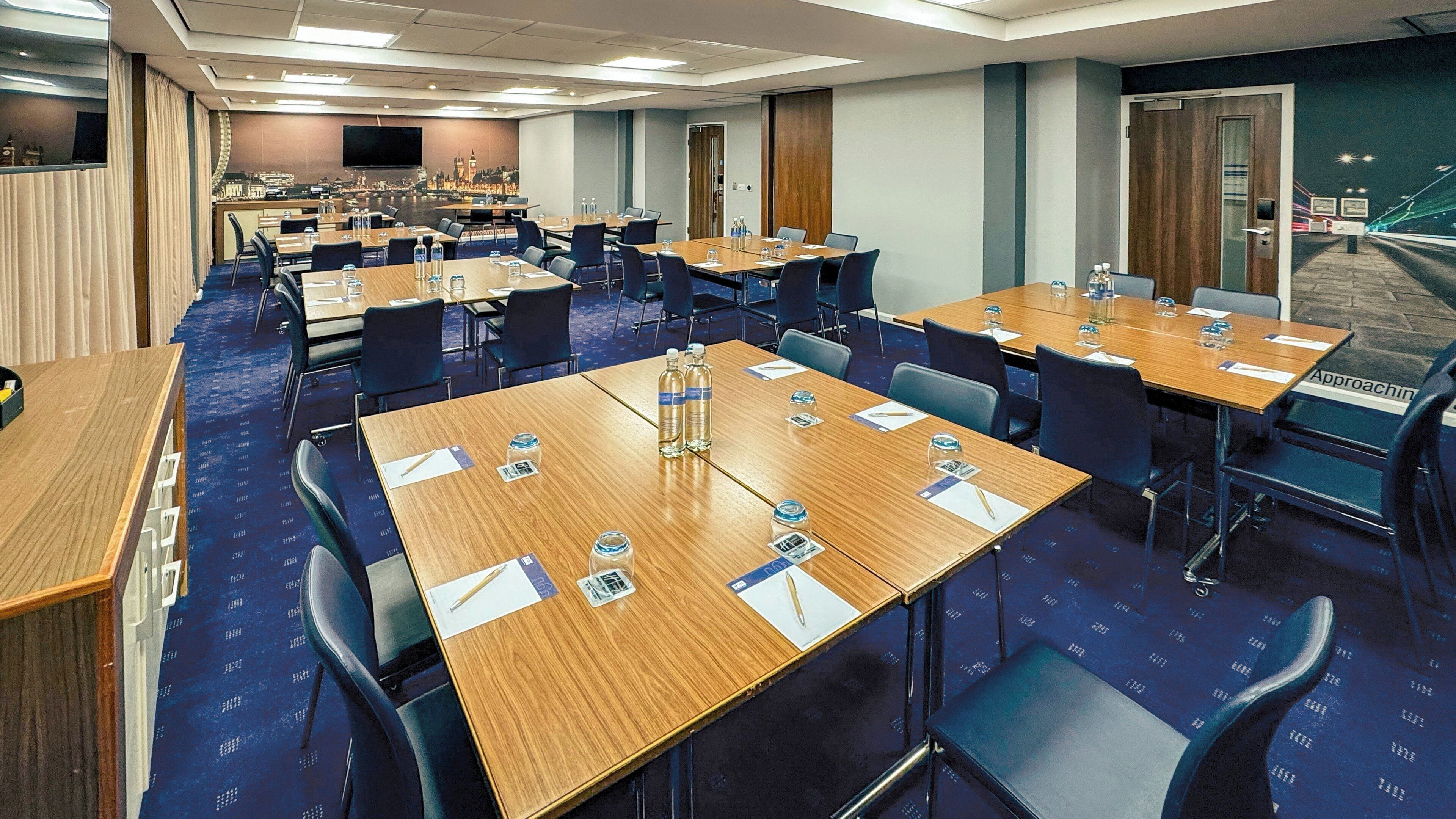 Un salón de conferencias con varias mesas, sillas y una pantalla grande.