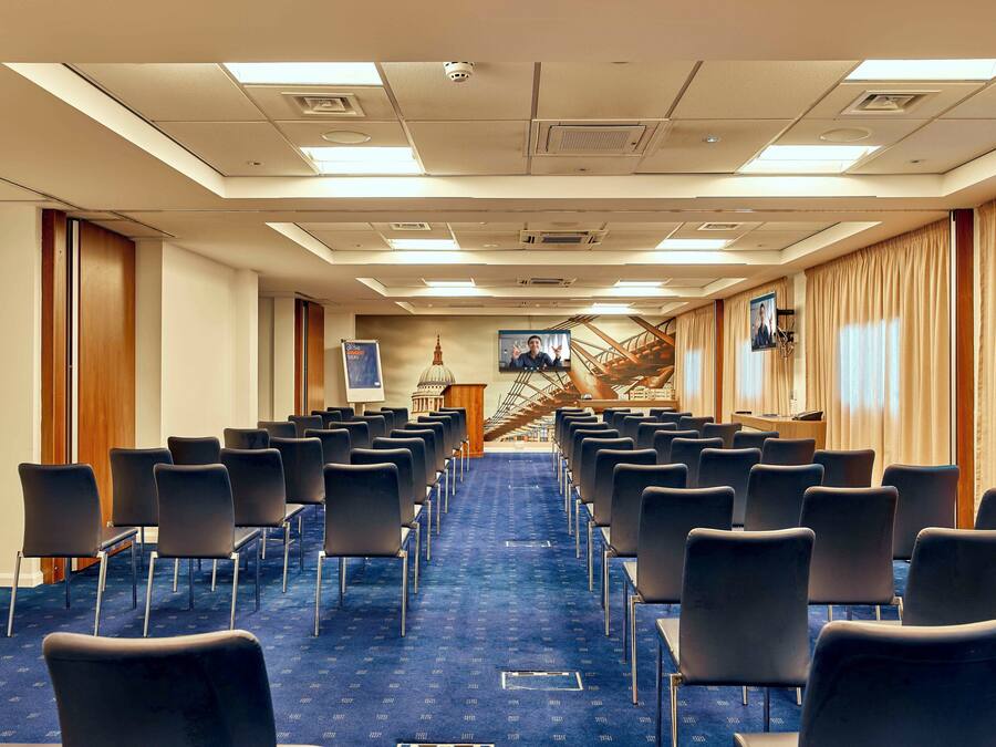 A conference room with rows of chairs, a podium, and a staircase.