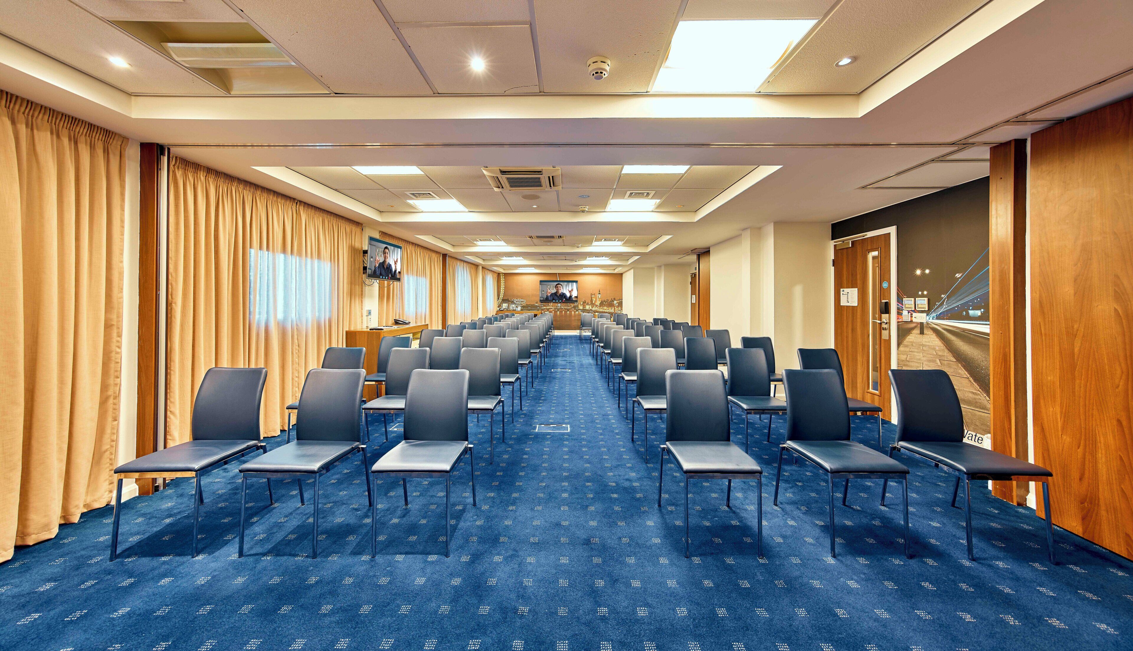 A conference room with rows of chairs, a podium, and a television screen.