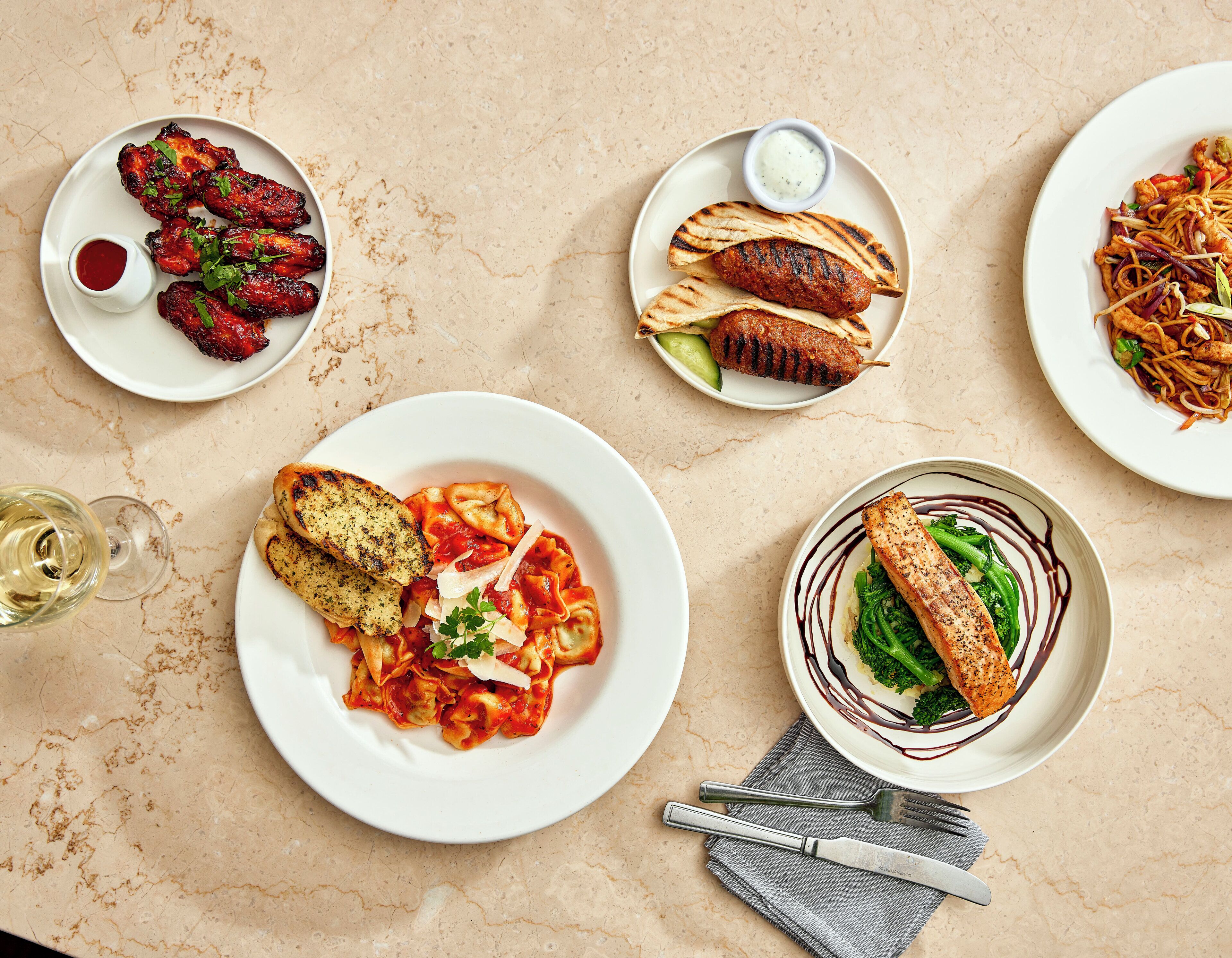 A table with various dishes, including pasta, grilled meats, and a fish fillet, suggesting a dining setting.