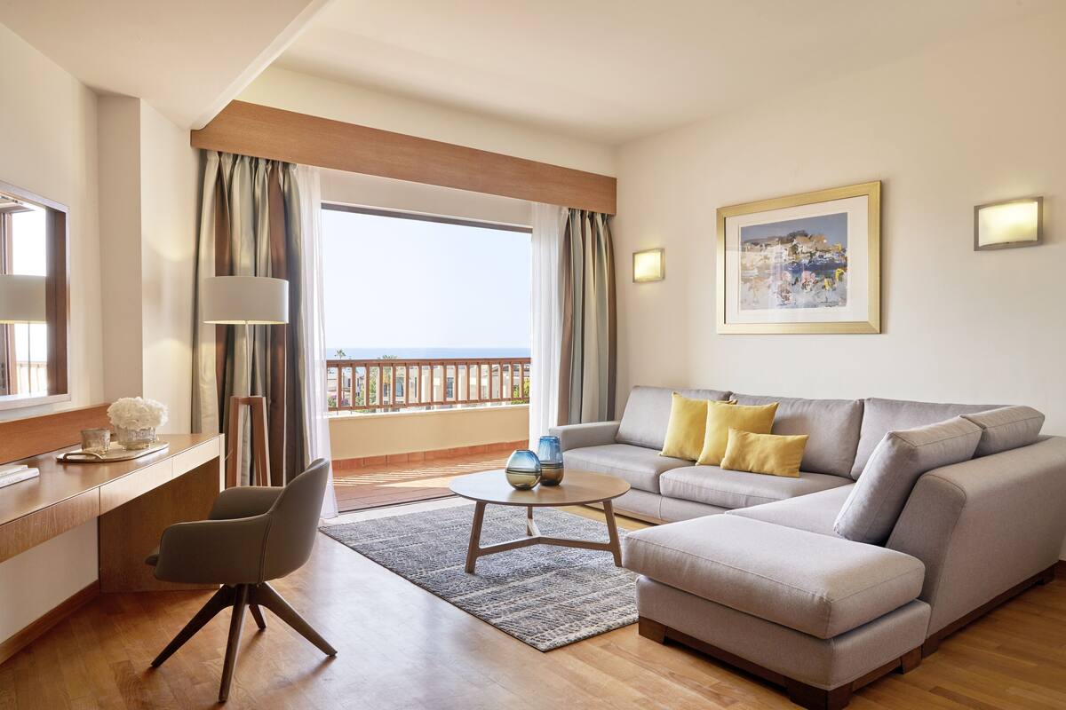 A modern hotel room with a balcony, a sofa, a desk, and a chair.