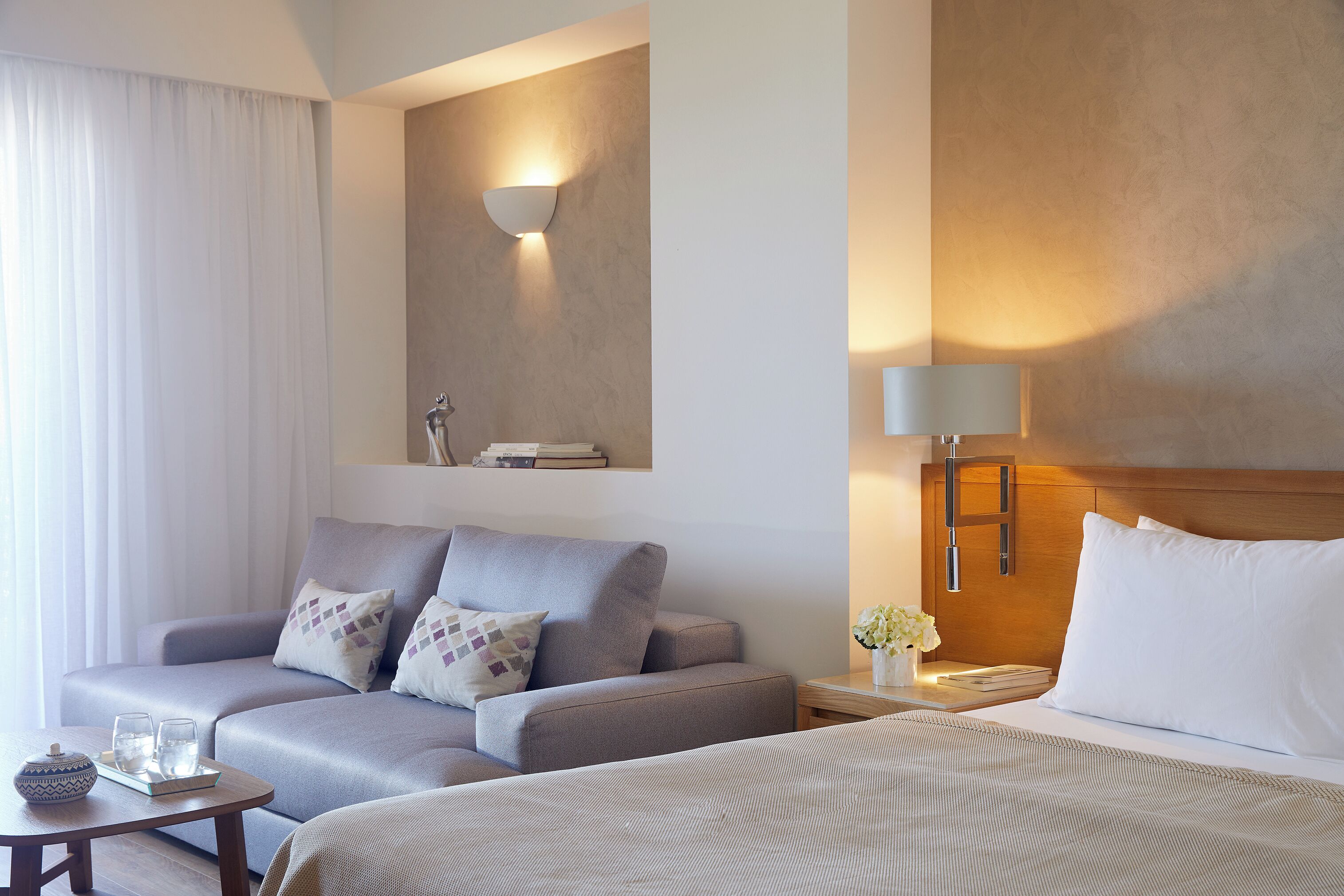 Une chambre d’hôtel équipée d’un canapé, d’un lit, d’une table de chevet et d’une lampe fixée au mur.