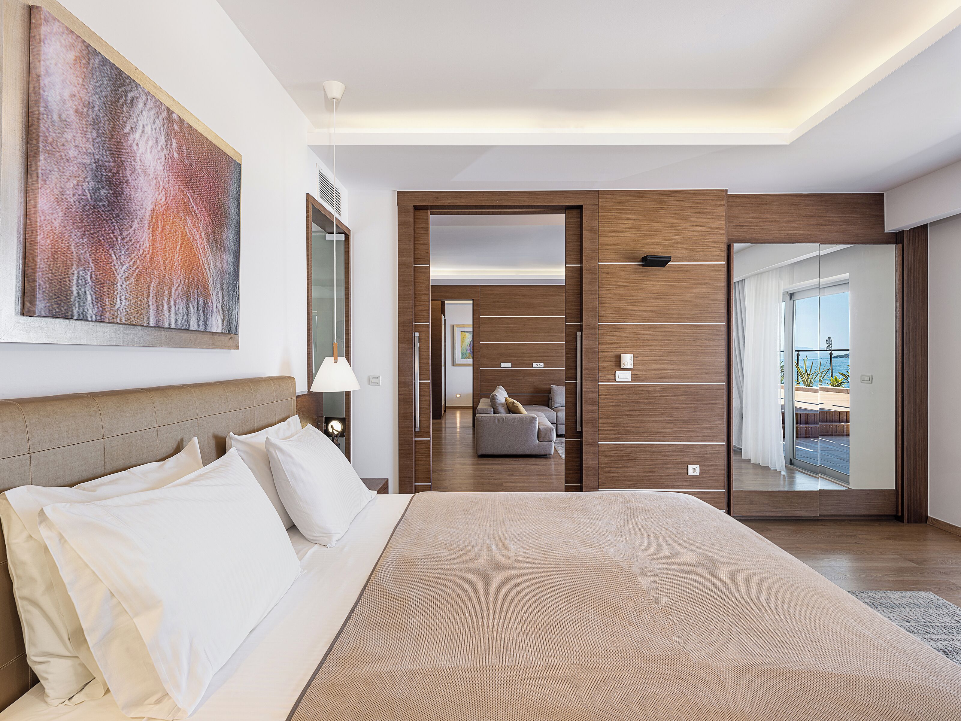 A modern hotel room with a large bed, a view of the sea, and a wooden accent wall.