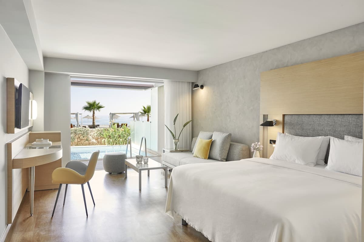 A modern hotel room with a large bed, a desk, and a view of the ocean.