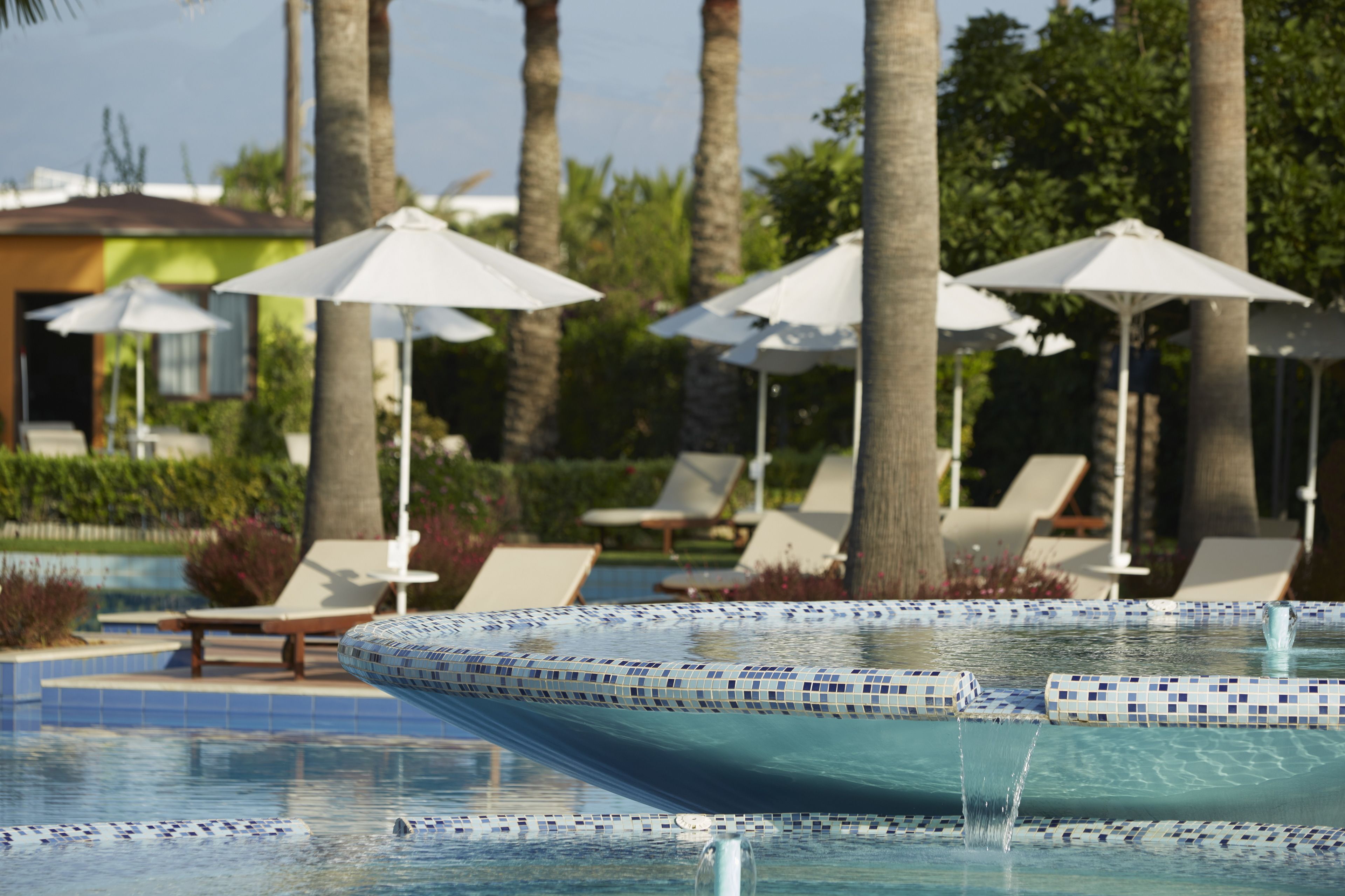 Un área de piscina con bordes de azulejos, sillas de descanso y sombrillas.