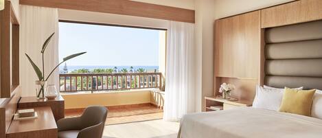 A hotel room with a large bed, a desk, a chair, and a balcony with a view of the ocean.