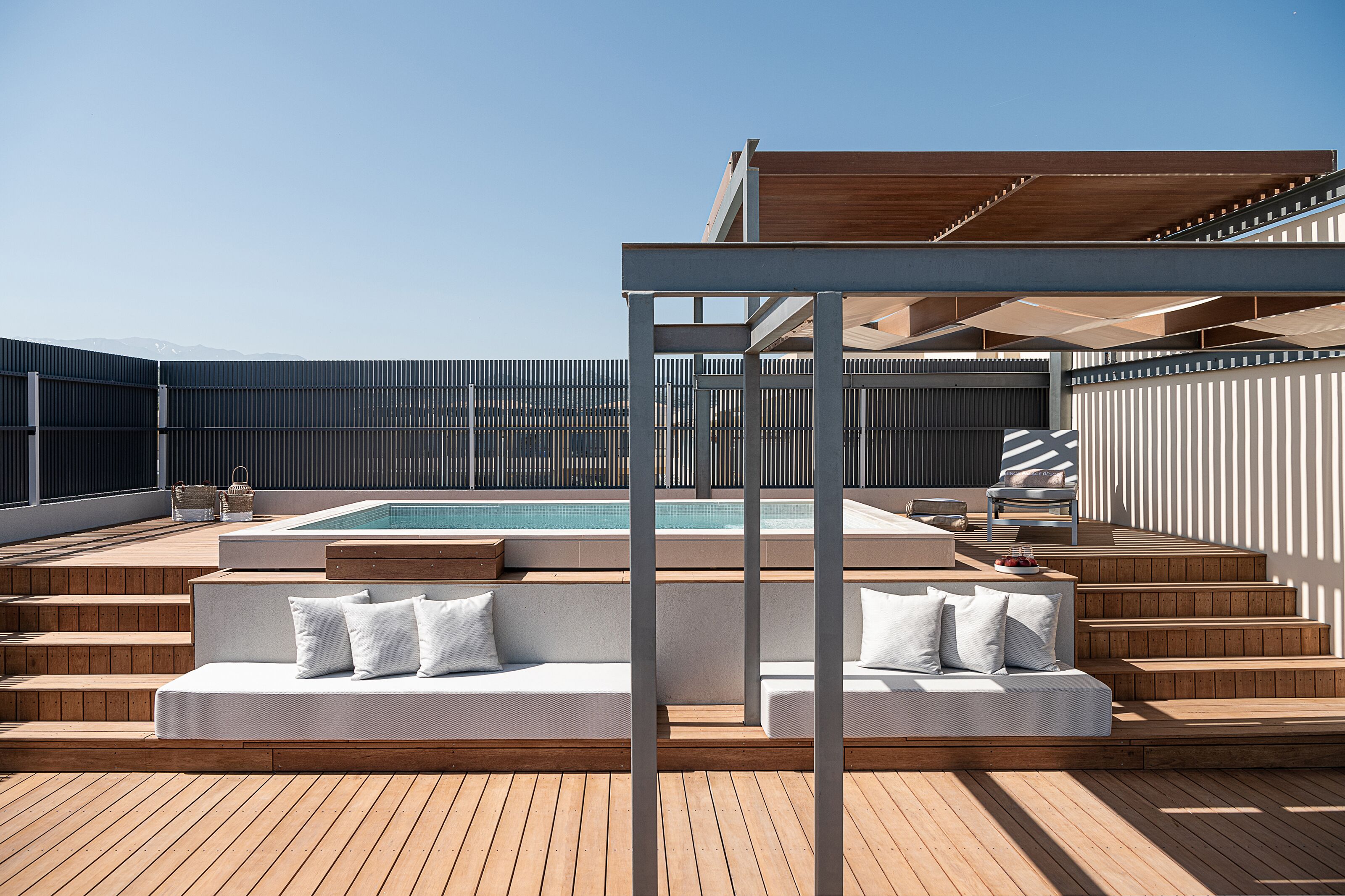 Um terraço no telhado com piscina, escadas de madeira e uma área de estar coberta.