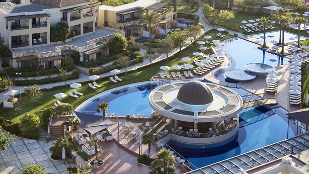 Un resort con una piscina grande, varias zonas de descanso y diversas opciones de asientos al aire libre.
