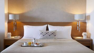 A neatly made hotel room with a large bed, two bedside lamps, a tray with breakfast items, and a decorative pillow.